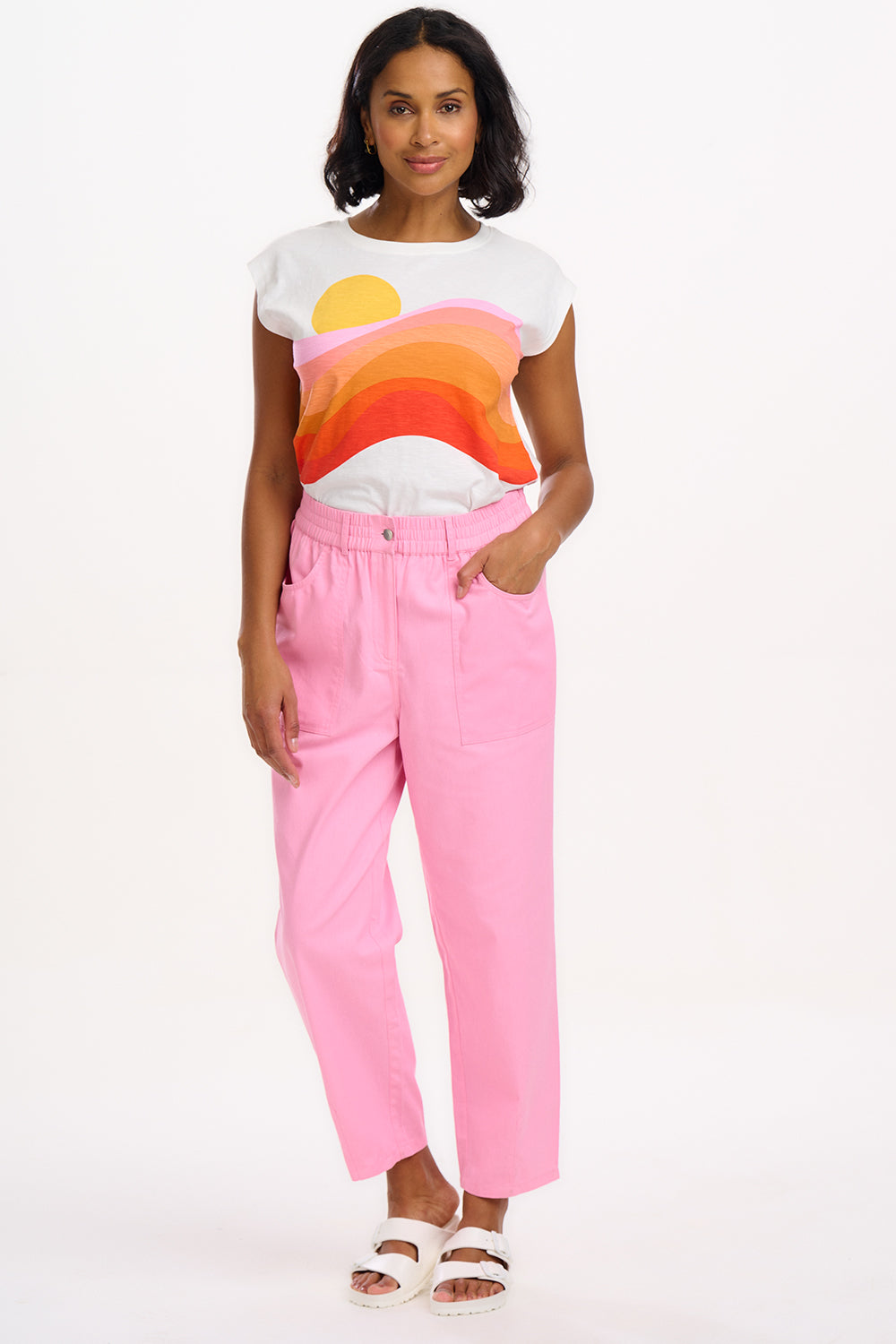 A model wearing pink Rowan trousers with a triple star pattern, paired with a striped top, standing against a white background.
