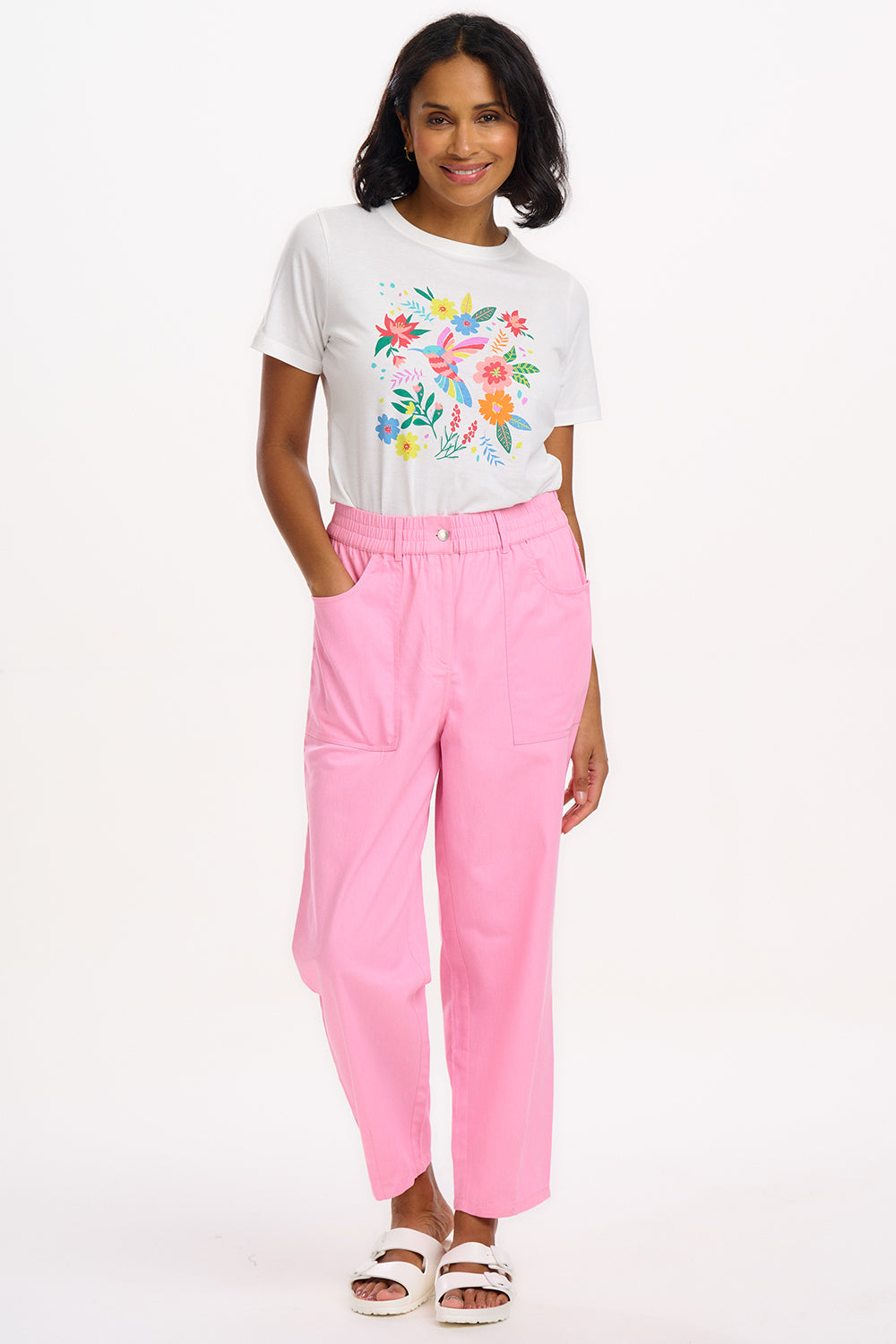 A model wearing a white t-shirt with a colorful floral design and pink trousers.