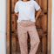 Woman wearing a white t-shirt with a red heart design and patterned pants standing in front of a wooden door.