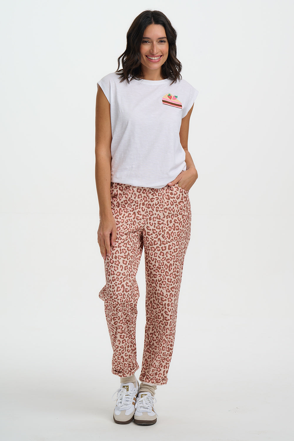 Woman wearing a white t-shirt with a graphic and pink leopard print pants on a white background