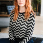Person wearing a black and white zigzag patterned sweater sitting on a couch.
