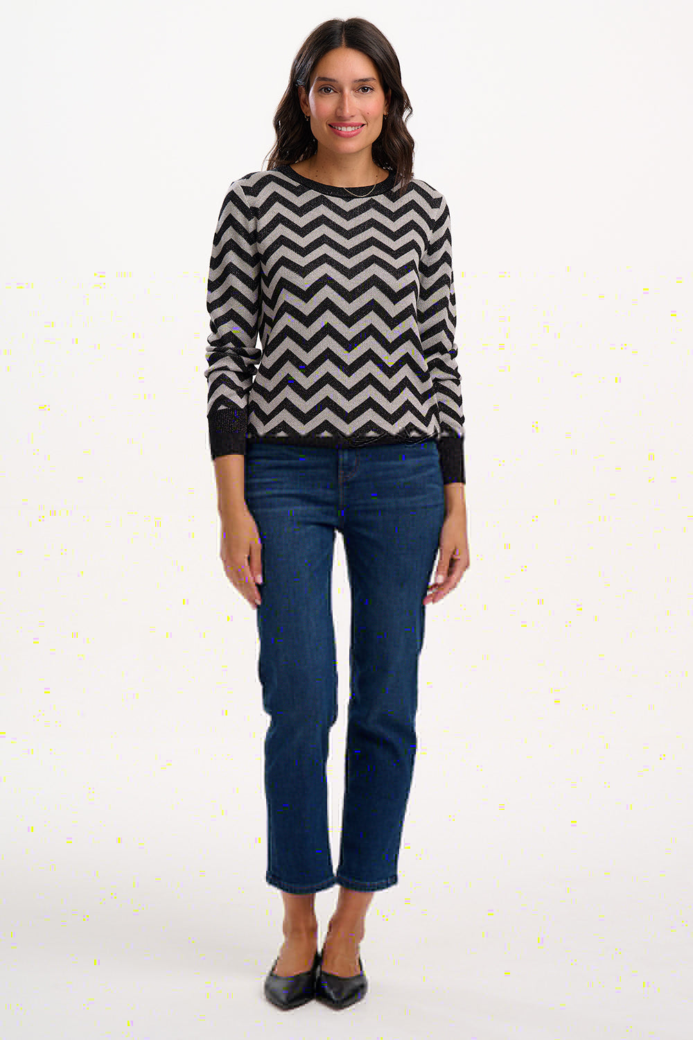 Woman wearing a black and white zigzag sweater and blue jeans on a white background