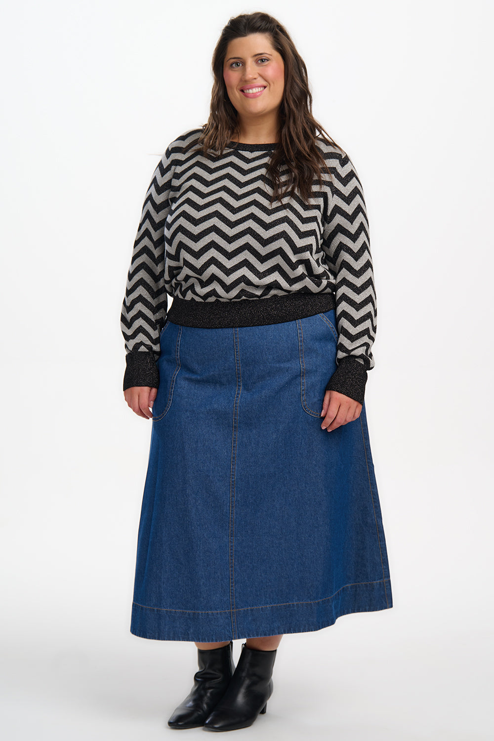 Woman wearing a black and white zigzag sweater with a blue denim skirt on a white background