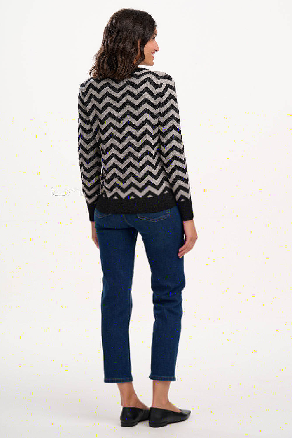 Woman wearing a black and white zigzag patterned sweater and blue jeans on a white background