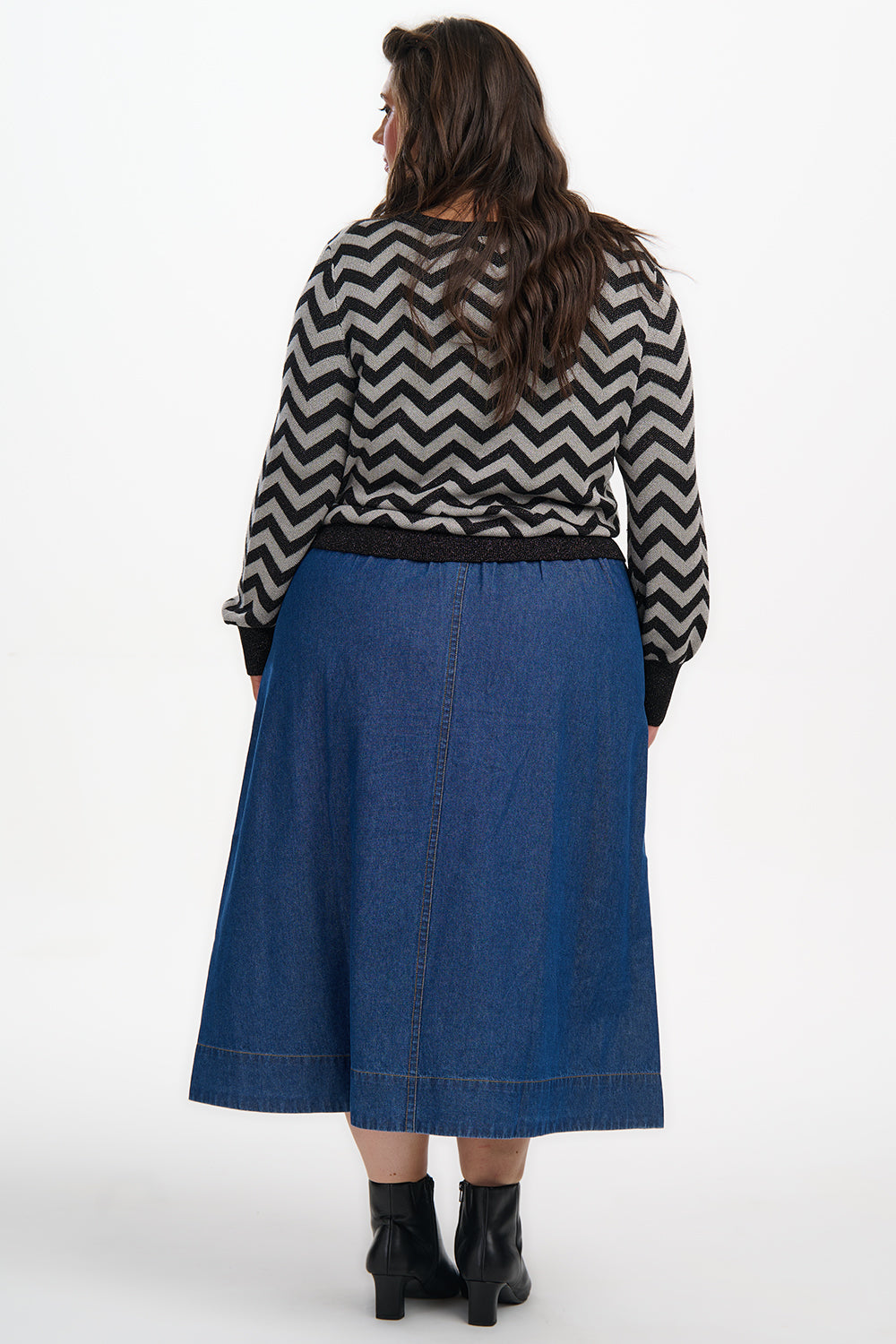 Person wearing a blue skirt and black and white zigzag patterned top on a white background