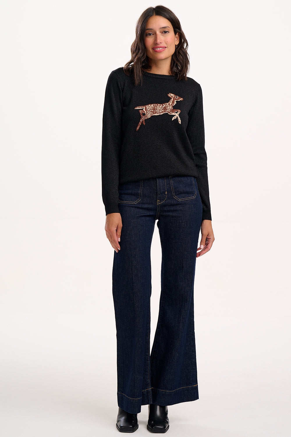 Woman wearing a black sweater with a graphic design and dark jeans on a white background