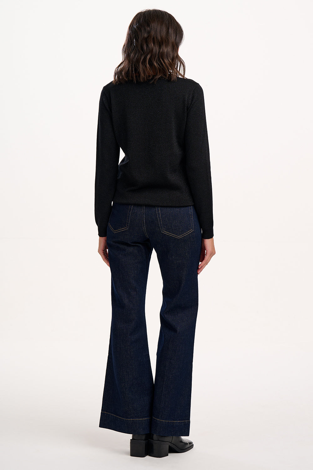 Person wearing a black sweater and dark blue jeans on a white background