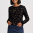 A woman modeling a black long-sleeve knit top with a brown leopard print pattern, paired with a blue denim mini skirt, against a light gray studio background.