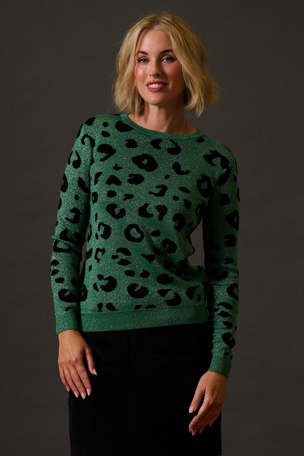 Woman wearing a green sweater with black leopard print pattern against a dark background
