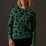 Woman wearing a green sweater with black leopard print pattern against a dark background