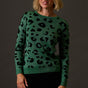 Woman wearing a green sweater with black leopard print pattern against a dark background