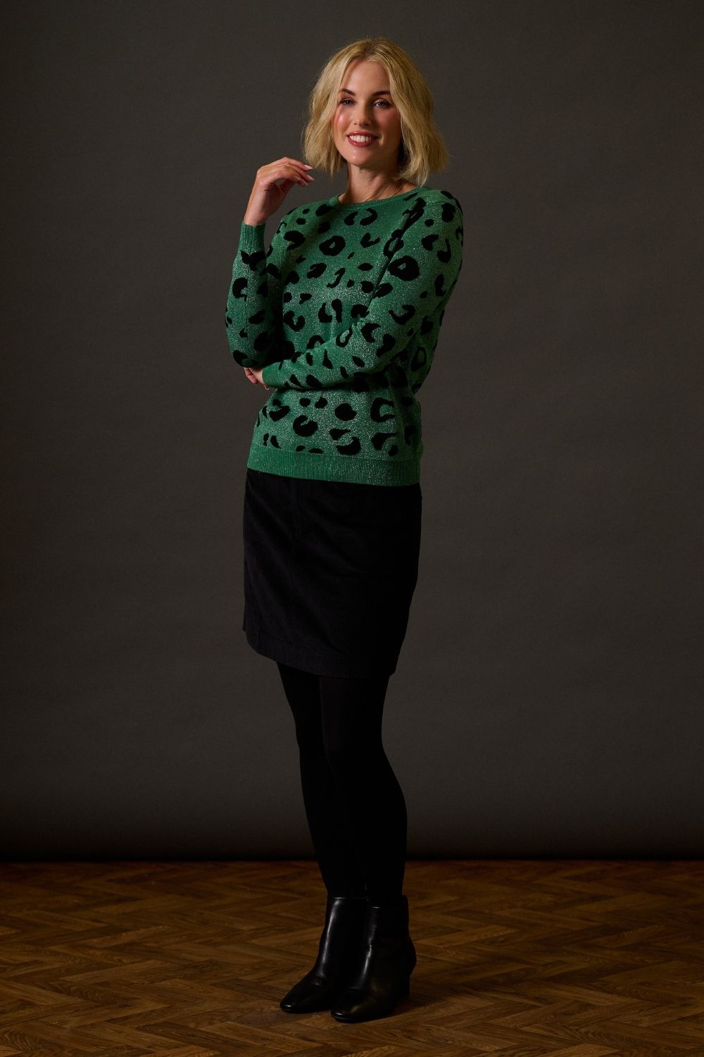 Woman wearing a green patterned sweater and black skirt against a dark background