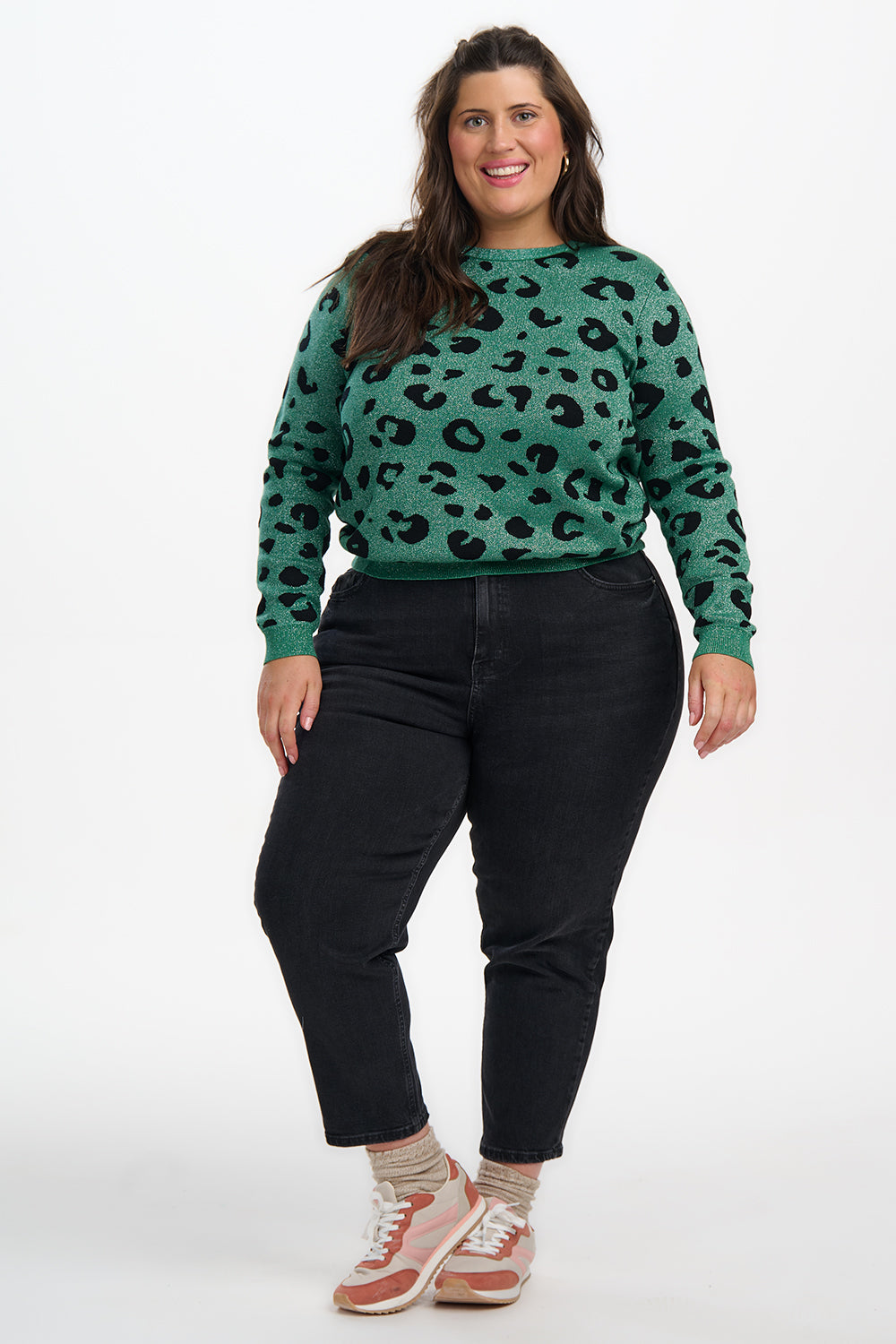 Woman wearing a green leopard print sweater and black pants on a white background