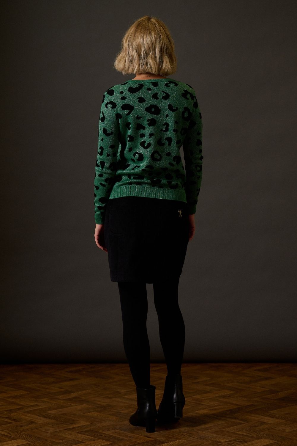 Person wearing a green sweater with black animal print pattern, standing against a dark background.