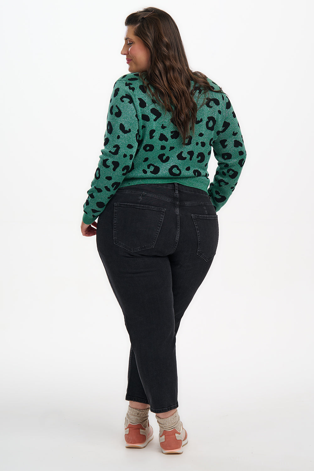 Person wearing a green leopard print sweater and black pants on a white background