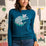Woman wearing a teal sweater with a cat design in front of a wall with cat-themed decorations.