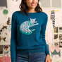 Woman wearing a teal sweater with a cat design in front of a wall with cat-themed decorations.