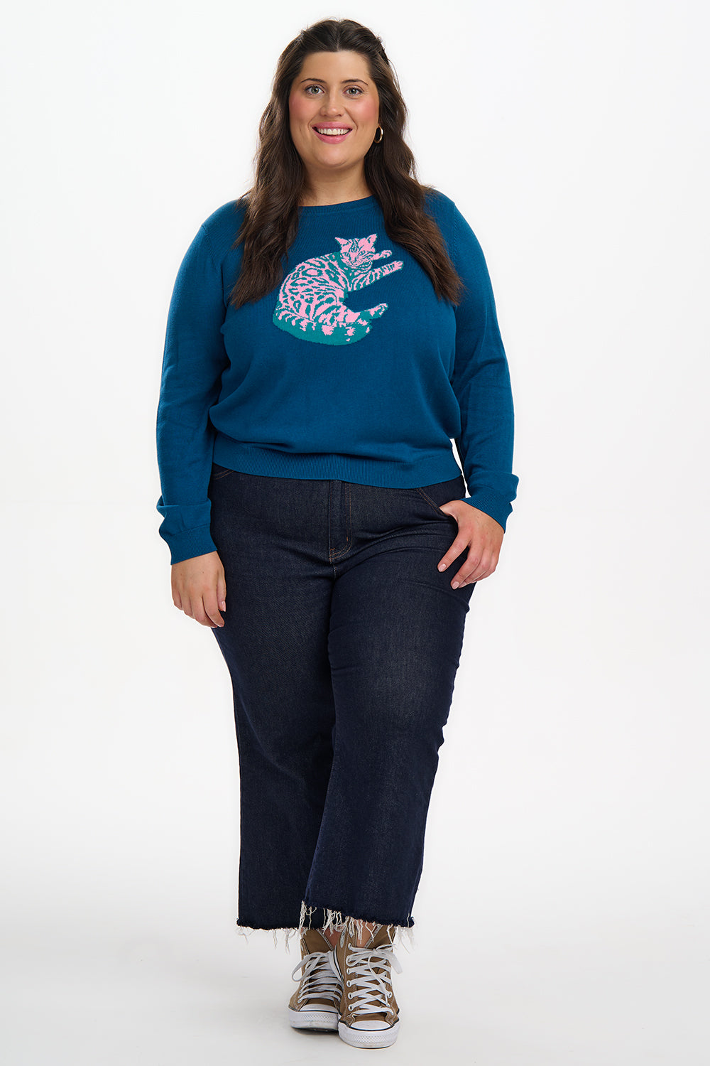 Woman wearing a blue sweater with a graphic design and dark jeans on a white background