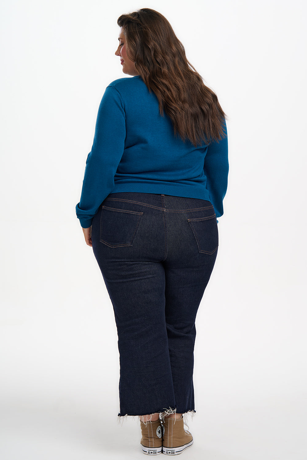 Person wearing a blue sweater and dark jeans on a white background