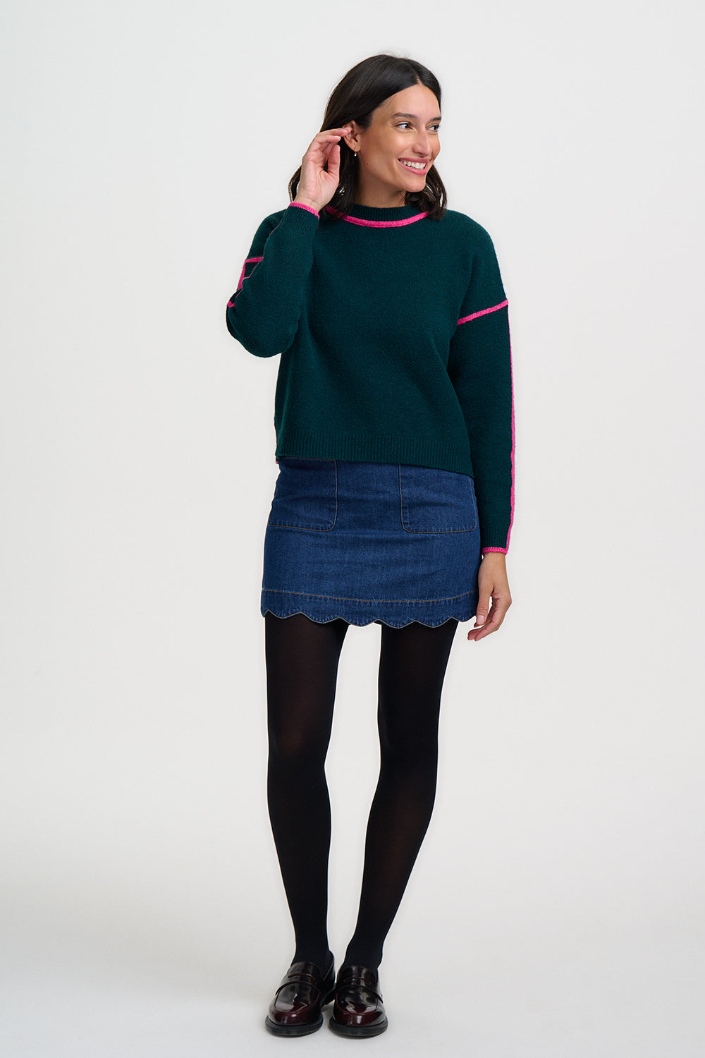 Woman wearing a green sweater with pink accents and a denim skirt on a white background