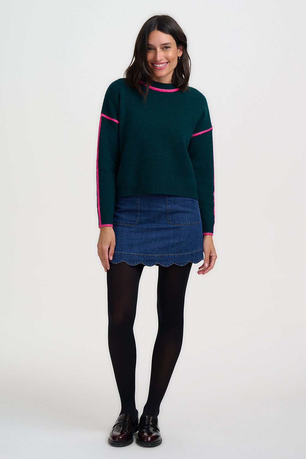 Woman wearing a green sweater with pink trim and a denim skirt on a white background