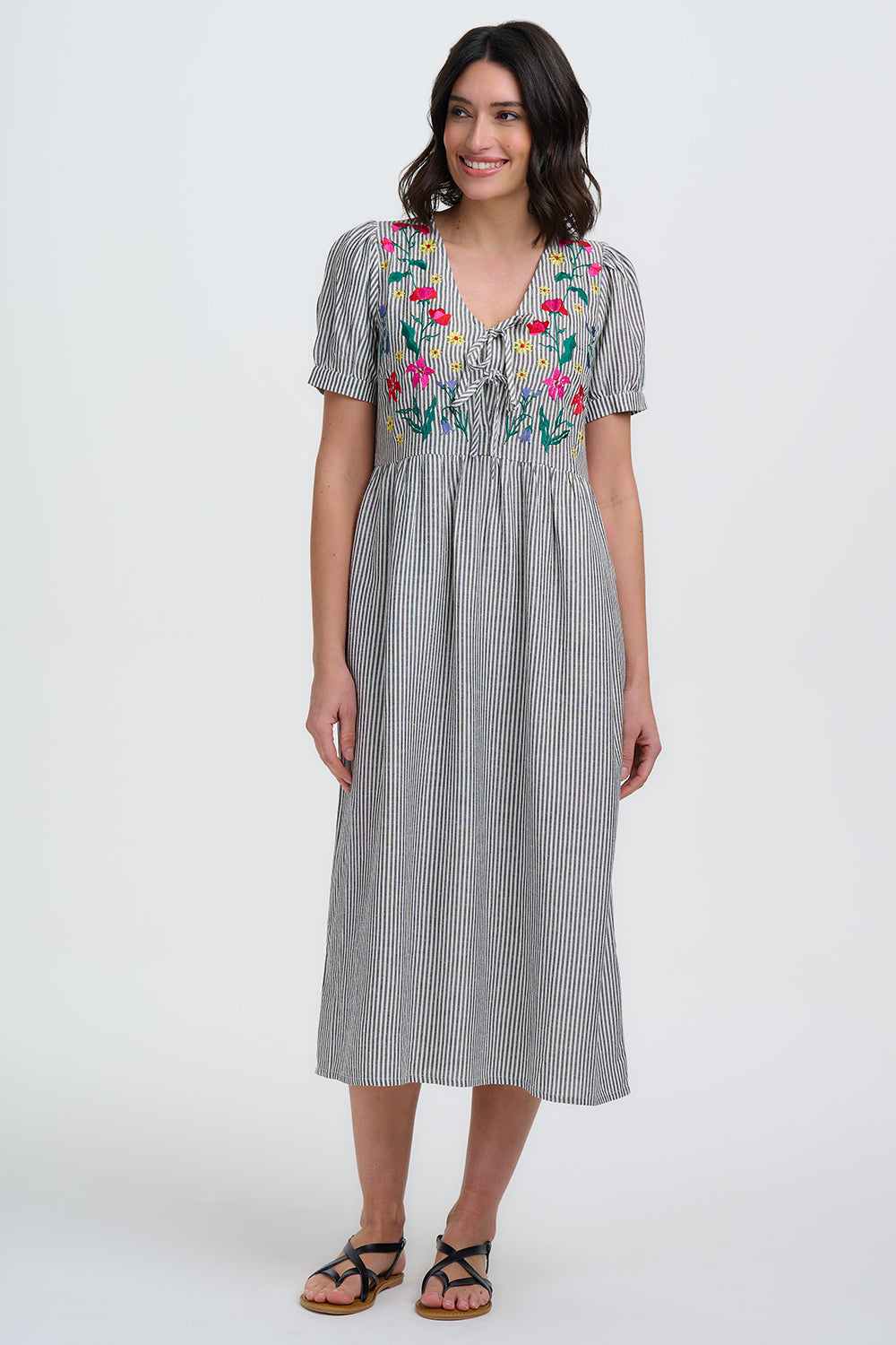 Woman wearing a gray striped dress with colorful floral embroidery on a white background