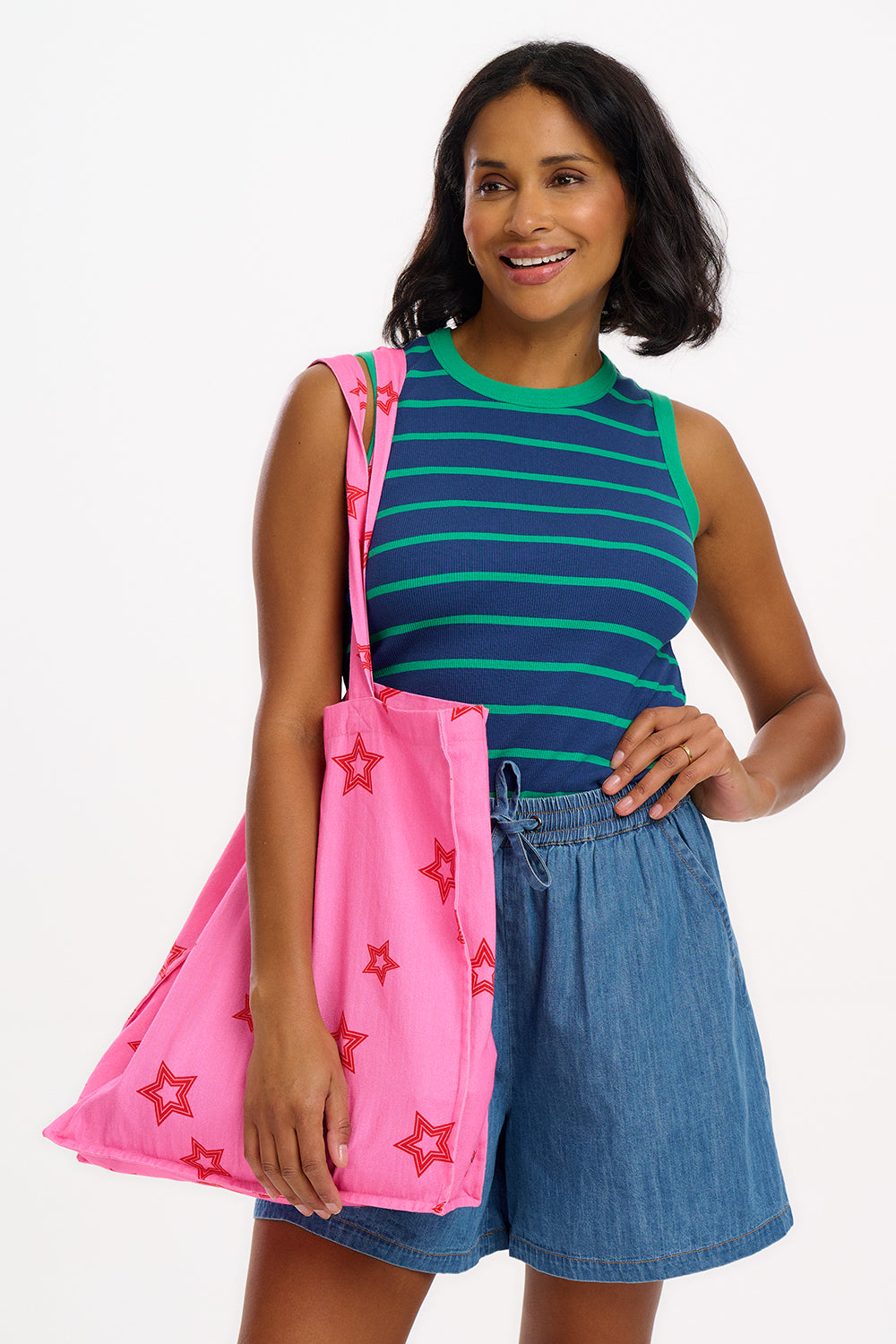 A woman wearing a sleeveless fitted vest top with blue and green stripes, paired with denim shorts and carrying a pink bag with stars.