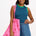 A woman wearing a sleeveless fitted vest top with blue and green stripes, paired with denim shorts and carrying a pink bag with stars.