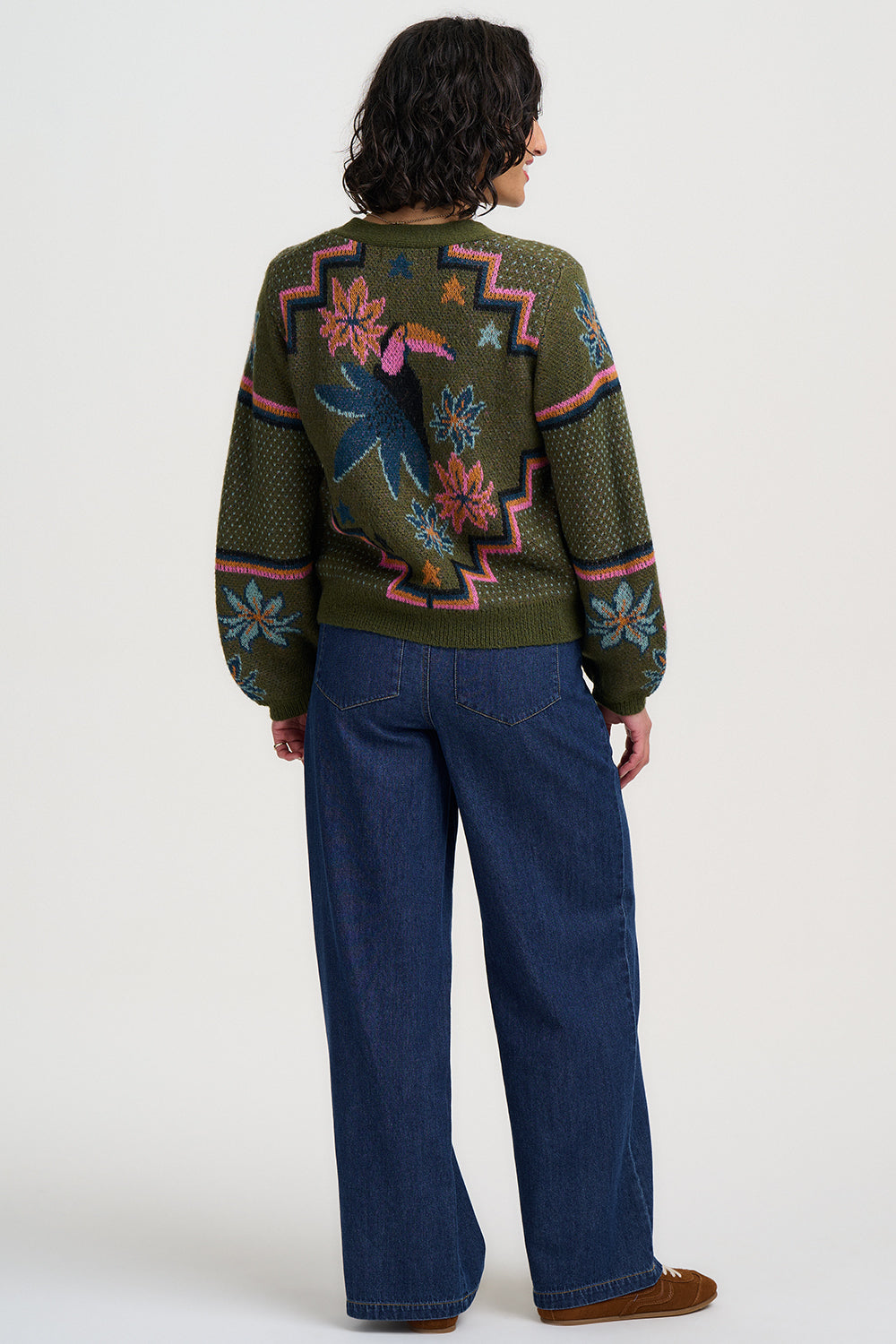 Person wearing a patterned sweater and blue jeans on a white background