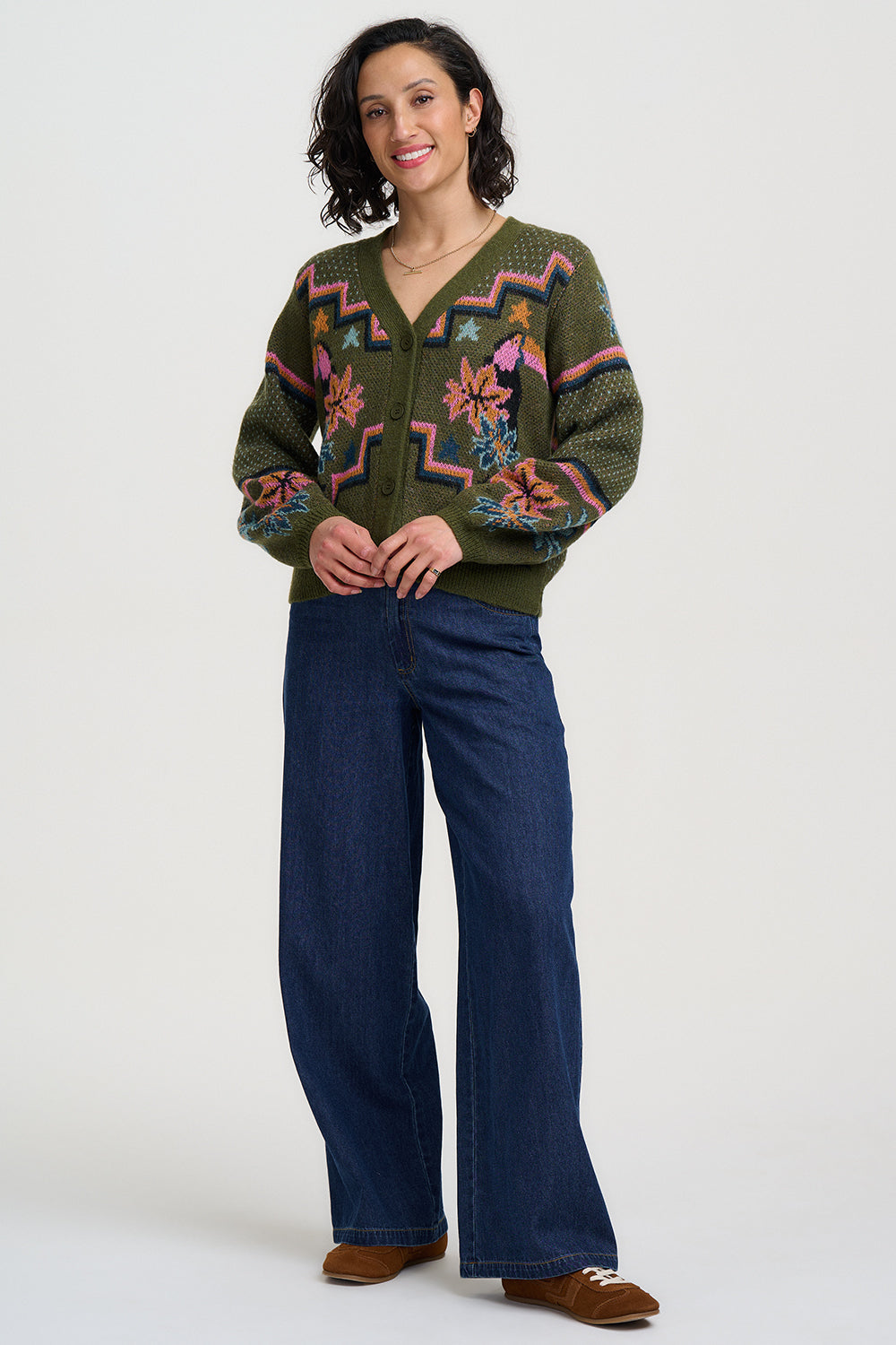 Woman wearing a patterned green sweater and blue jeans on a white background