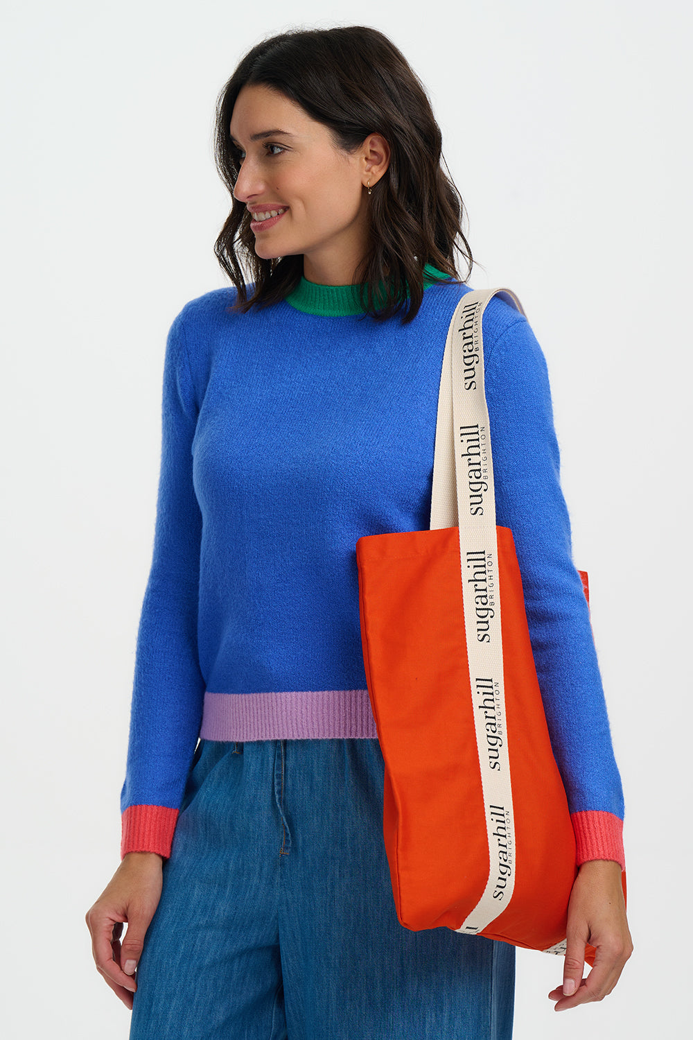 Woman holding an orange tote bag with a visible brand logo against a white background