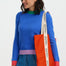 Woman holding an orange tote bag with a visible brand logo against a white background