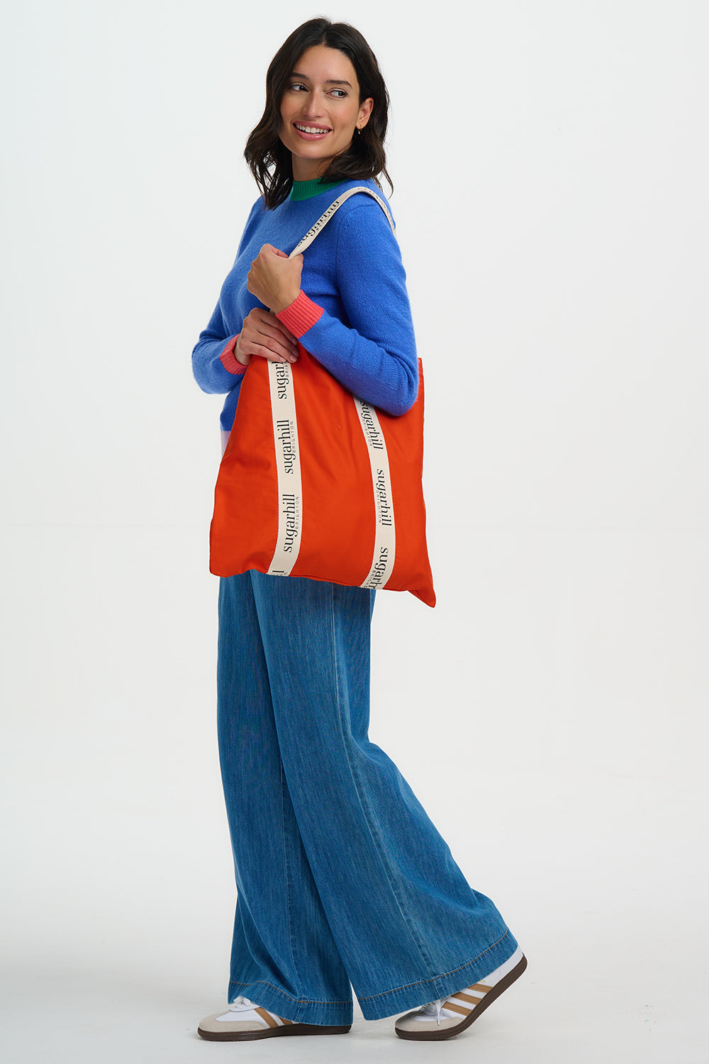 Woman holding an orange tote bag with a white strap against a white background