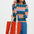 Woman holding a red tote bag with white text, wearing a colorful checkered top and blue pants on a white background