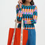 Woman holding a red tote bag with white text, wearing a colorful checkered top and blue pants on a white background