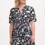 A woman wearing a knee-length V-neck dress with short sleeves and a tiered skirt. The dress features a black and white floral folk print.