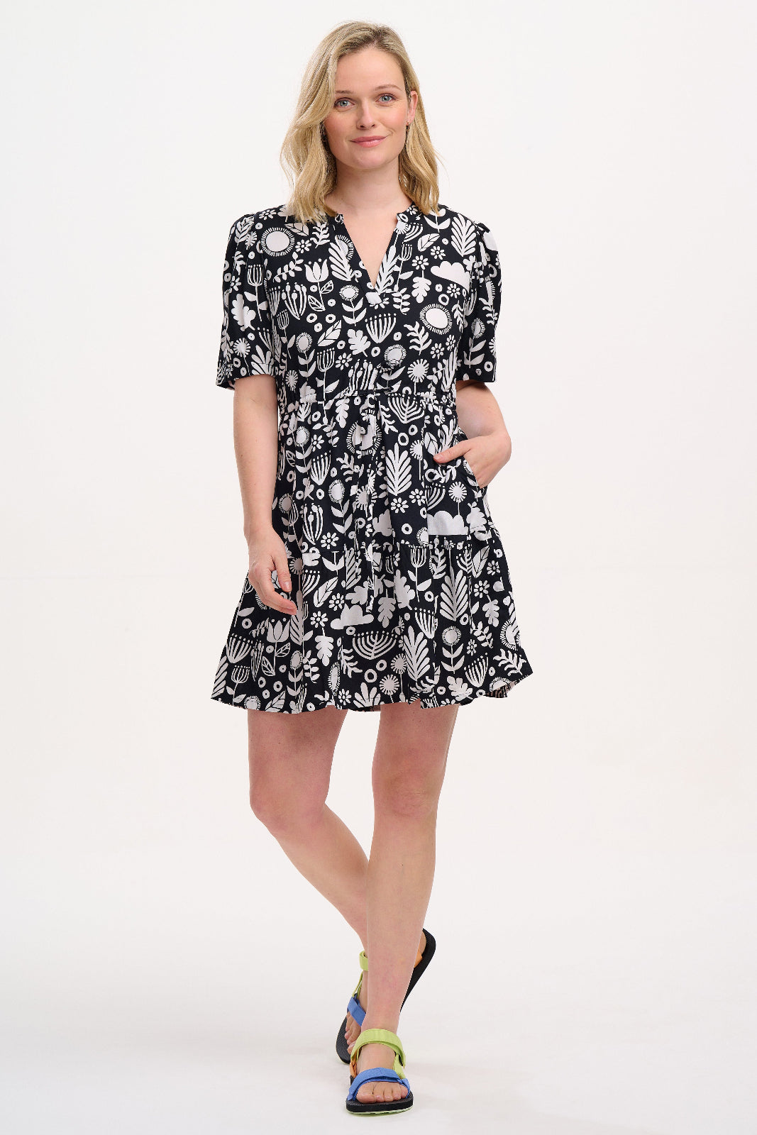 A woman wearing a knee-length V-neck dress with short sleeves and a tiered skirt. The dress features a black and white floral folk print.