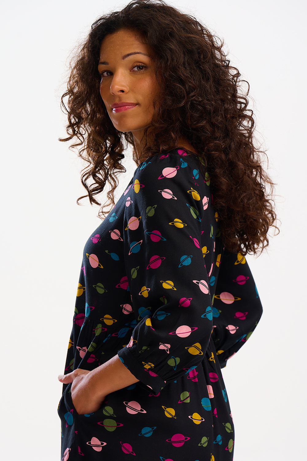 A woman standing, wearing a midi smock dress with a colorful planet pattern on a black background, paired with black boots.