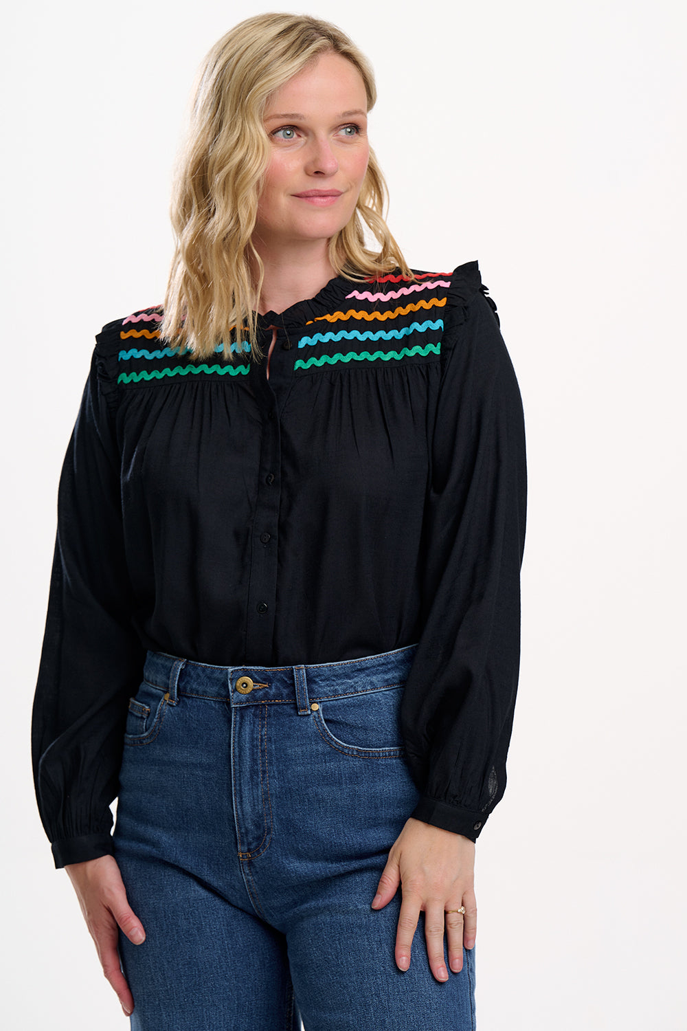 Woman wearing a black blouse with colorful accents and blue jeans on a white background