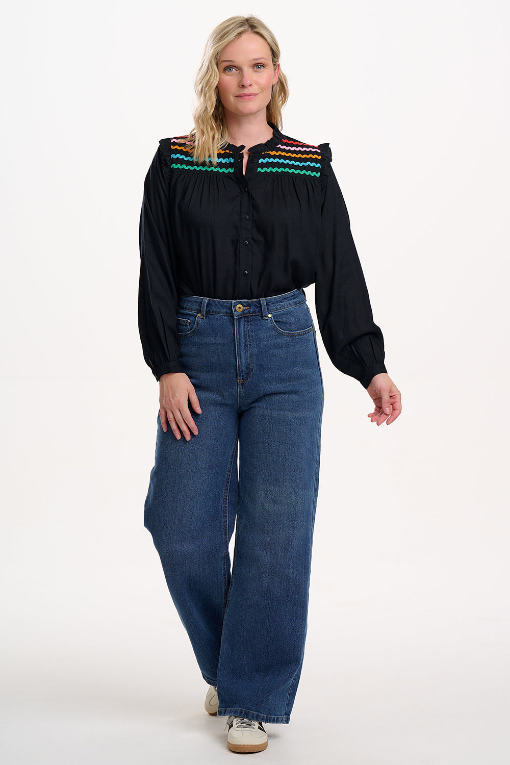 Woman wearing a black blouse with colorful accents and blue jeans on a white background