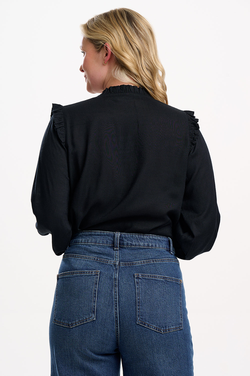 Person wearing a black blouse with ruffled shoulders and blue jeans on a white background