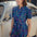 A person smiling and wearing a blue mini shirt dress with a geometric broken lines pattern.