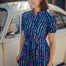A person smiling and wearing a blue mini shirt dress with a geometric broken lines pattern.