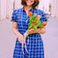 Woman in a blue checkered dress holding tulips on a street.