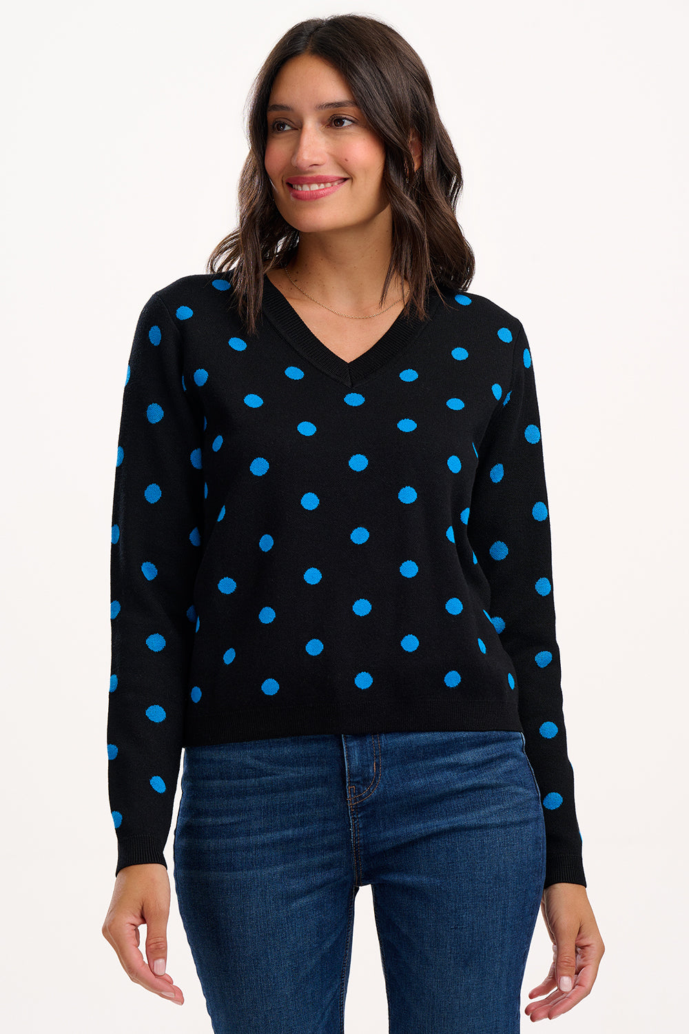 Woman wearing a black sweater with blue polka dots and blue jeans on a white background