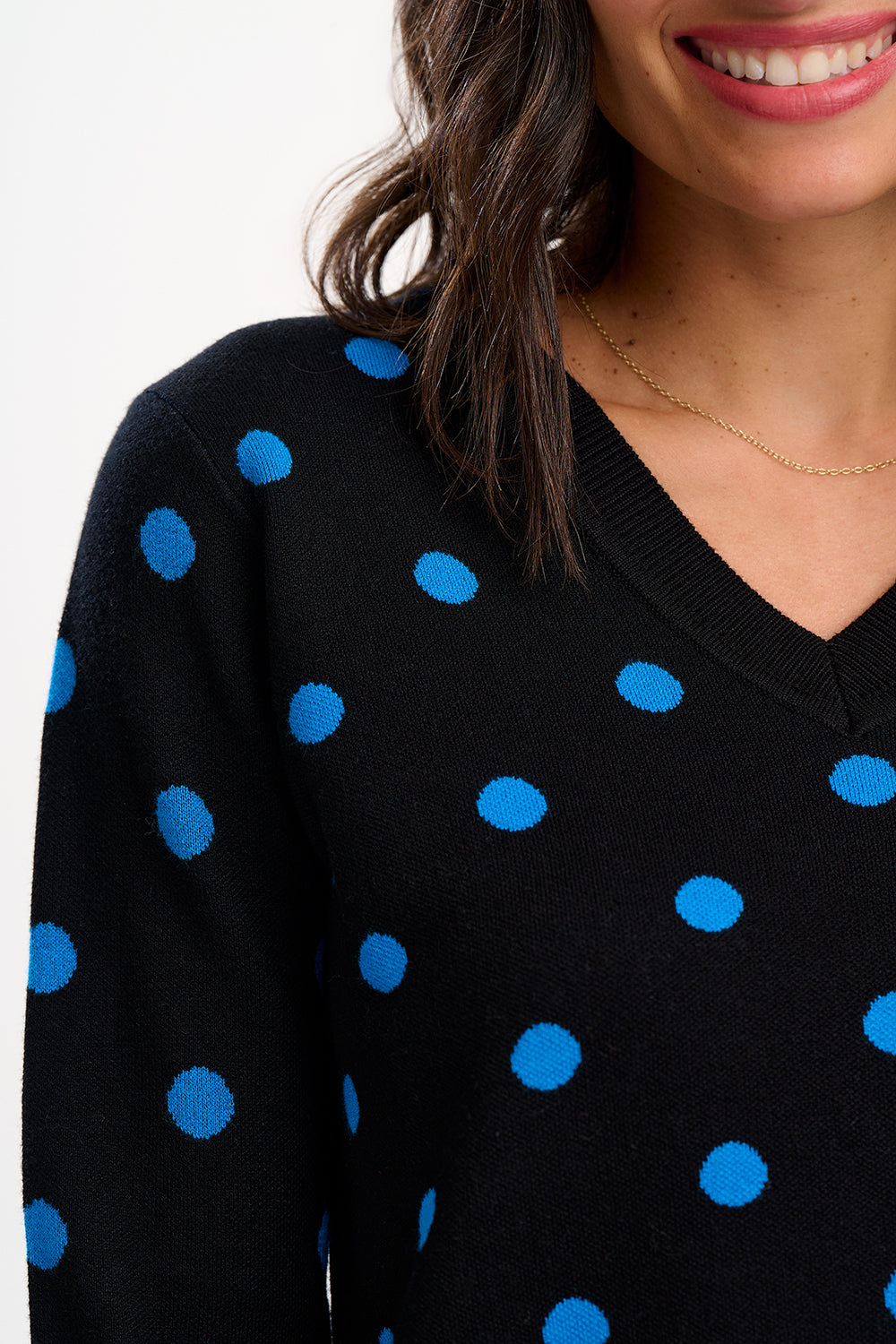 Black sweater with blue polka dots worn by a person on a white background