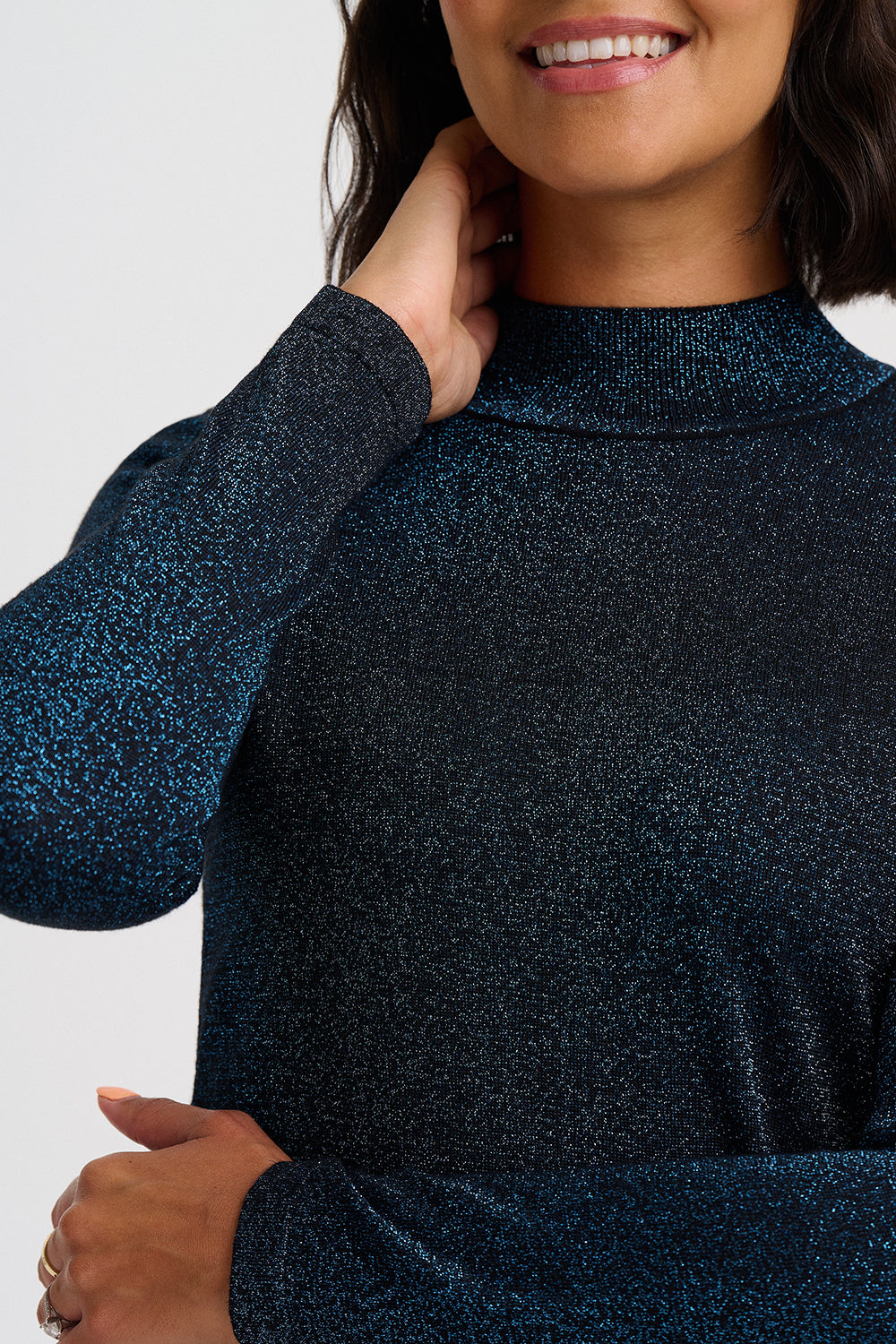 A close-up of a woman wearing a dark navy blue long-sleeve mock neck sweater with a subtle glittery texture, set against a plain light gray background.
