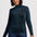 A woman wearing a dark teal long-sleeve mock neck knit sweater and dark blue jeans, standing against a light gray studio background.