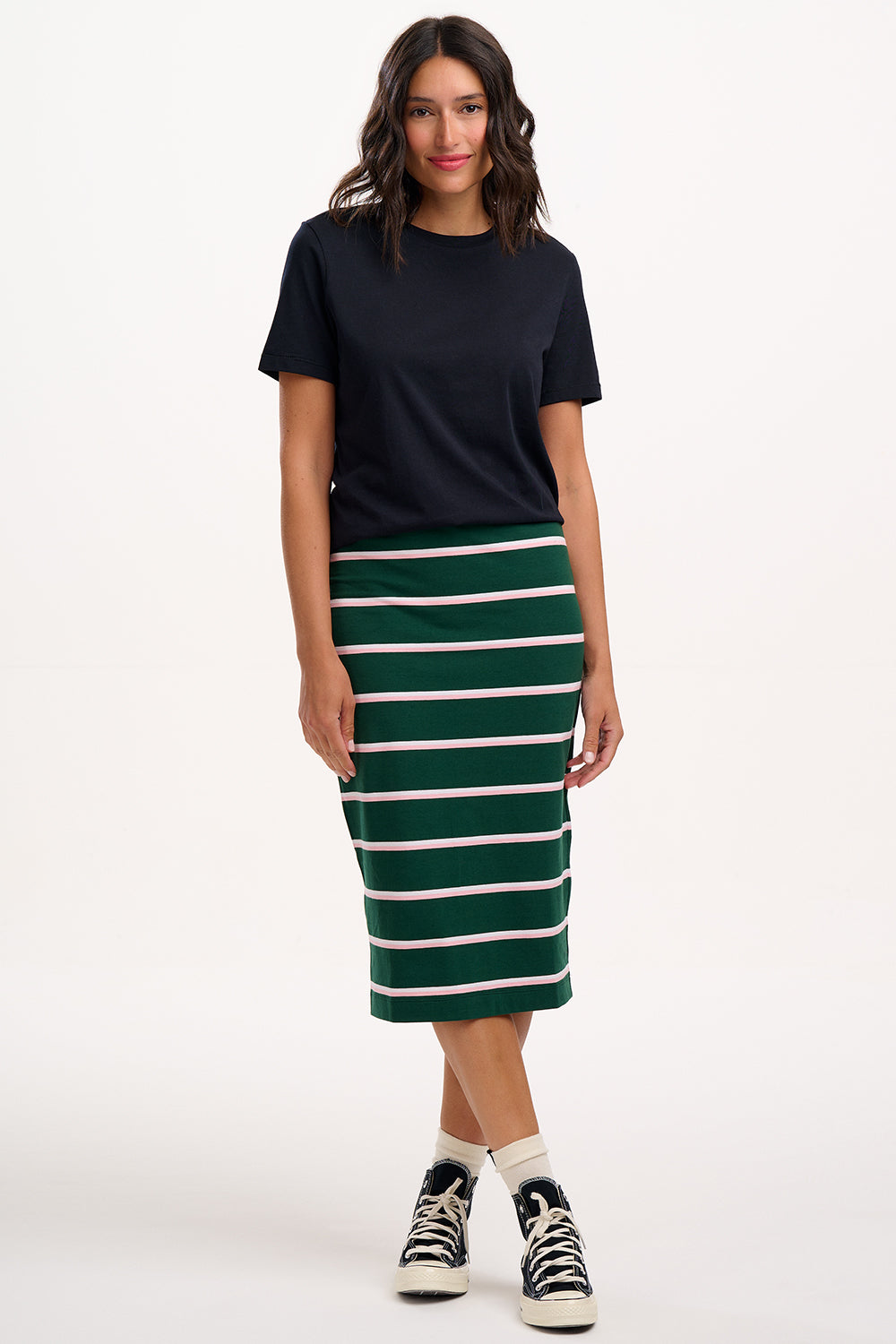 Sugarhill brighton model wearing a black t-shirt and green striped skirt on a white background