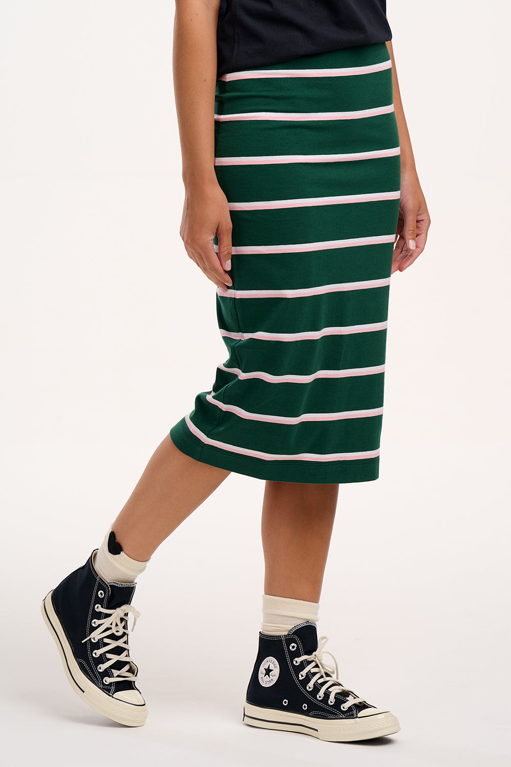 Sugarhill Brighton model wearing a green and white striped skirt with black Converse shoes on a white background